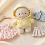 黄色いパーカーを着た棉花娃娃（ぬい）と、ミニサイズのワンピース・カーディガン・スカートを平置きした写真